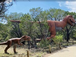 Two life-size dinosaur statues in a green forest atmosphere